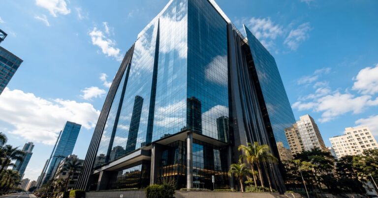 Edifício comercial moderno com fachada espelhada refletindo o céu azul, representando investimentos imobiliários.