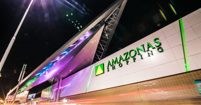 Fachada noturna iluminada do Amazonas Shopping com pessoas circulando pela entrada principal