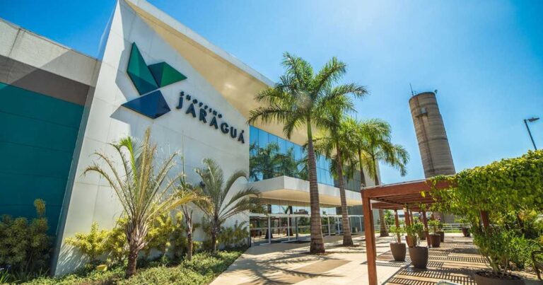 Fachada externa moderna e ensolarada de um shopping center cercada por palmeiras