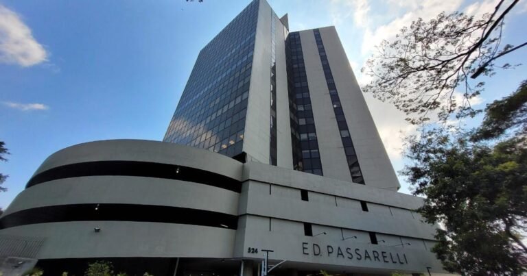 Fachada de prédio comercial envidraçado representando o Edifício Passarelli, com pessoas circulando em dia ensolarado.